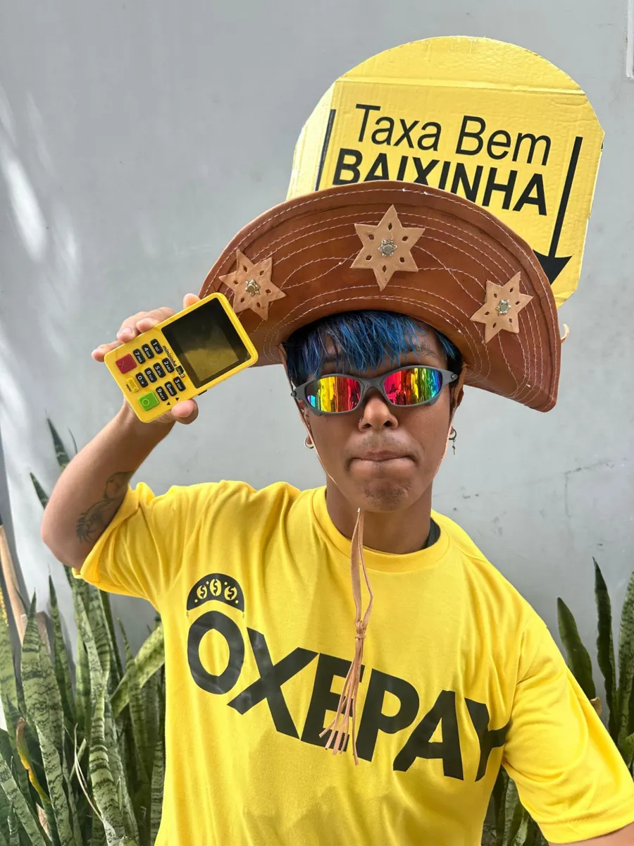 Rapaz de chapéu de couro e camiseta OxePay segurando a OxeMini amarela