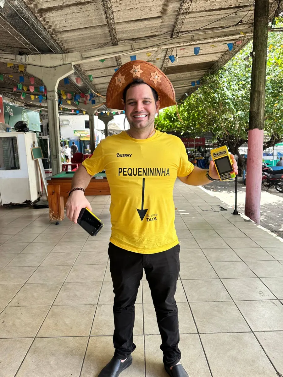 Rapaz sorrindo com camiseta Pequenininha, eu disse taxa, segurando a OxeSmart